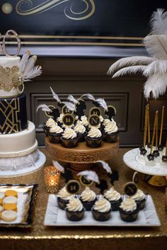 a table topped with cupcakes and cakes covered in frosting next to feathers