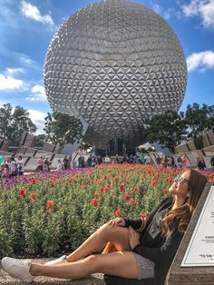 a woman sitting on a bench in front of a flower garden with a large ball behind her