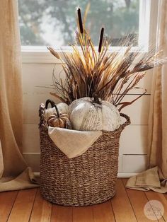 a wicker basket filled with pumpkins and other fall decorations in front of a window