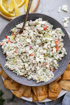 a bowl filled with chicken salad next to crackers and lemon wedges on a table