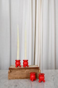 three red candles sitting on top of a wooden box next to two white candles in front of a curtain