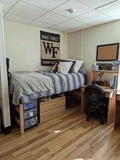 a bedroom with a bed, desk and computer on top of wooden drawers in front of a white wall