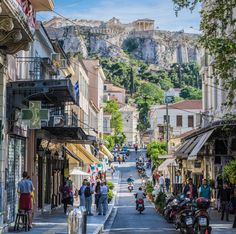 people are walking down the street in front of some buildings and an ancient hill behind them