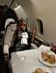 a woman is sitting on an airplane with food and drinks in front of her face