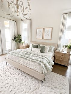 a large white bed sitting in a bedroom under a chandelier next to two windows