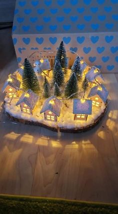 a lit up christmas village with houses and trees in the snow on a wooden table