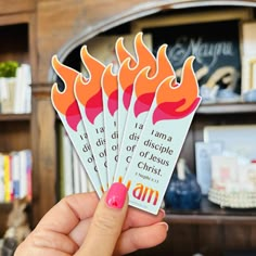 a person holding up four stickers with flames on them in front of a book shelf