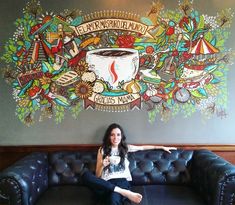 a woman sitting on top of a couch in front of a wall with a mural