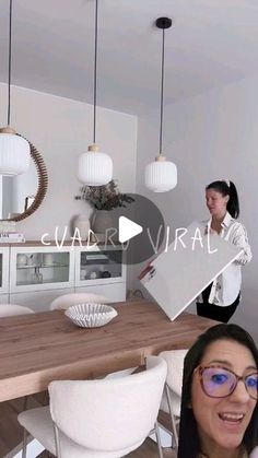 a woman standing in front of a wooden table with white chairs next to a kitchen