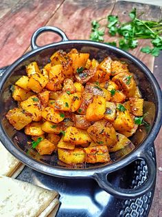 a pan filled with potatoes and bread on top of a wooden table next to some parsley