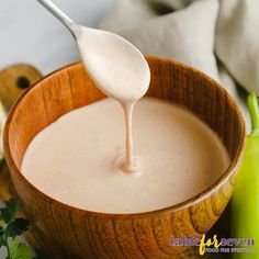 a wooden bowl filled with white sauce and garnished with parsley on the side