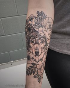 a woman's arm with a wolf and flowers tattoo on her left arm, next to a brick wall