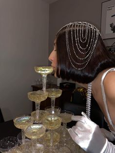 a woman in white gloves and pearls on her head is looking at a display of wine glasses