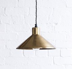 a brass pendant light hanging from a white brick wall with a black cord attached to it