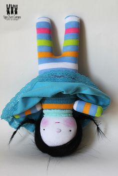 a stuffed animal wearing a blue dress and striped socks on it's head with its eyes closed