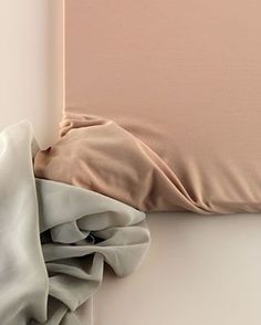 an unmade bed with two sheets and a pillow on it's side, in front of a white wall