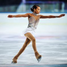 a female figure skating on the ice in a short white dress with sequins