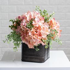 pink flowers are in a black vase on a white table