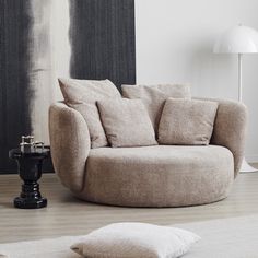 a living room with a round couch and pillows on the floor next to a lamp