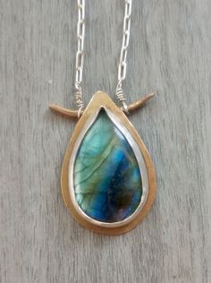 Large blue labradorite teardrop shape cabochon in a bronze and silver bezel setting on long silver chain chain necklace. The gemstone is natural with the gorgeous rainbow colored light flashes that labradorite is famous for: labradorescence. The labradorite  The labradorite stone is about 1 inch long and 0.6 inch wide. The pendant is about 1.25 inches long and about 0.75 inch wide. The necklace will arrive in a simple gift box with hemp flower ribbon, ready as a gift. The necklace is made out of Unique Nickel-free Teardrop Necklaces, Artisan Bronze Teardrop Jewelry, Silver Labradorite Teardrop Necklace, Silver Oval Electroformed Necklace, Unique Hand Forged Long Drop Jewelry, Silver Labradorite Drop Jewelry, Wire Wrapped Teardrop Brass Necklaces, Unique Hand Forged Teardrop Pendant Jewelry, Unique Nickel-free Necklace With Teardrop Pendant