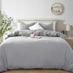 a bed with grey sheets and pillows in a bedroom next to a plant on the floor