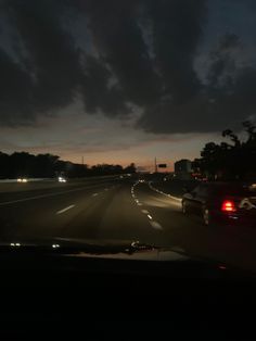 cars driving down the road at night time with dark clouds in the sky behind them