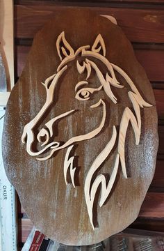 a horse head carved into a wooden plaque on top of a book shelf next to a pile of books