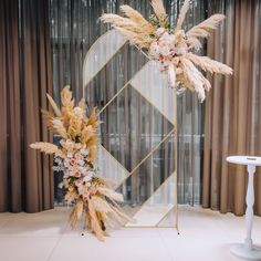 two tall white flowers are on display in front of a gold and glass mirror with curtains behind it