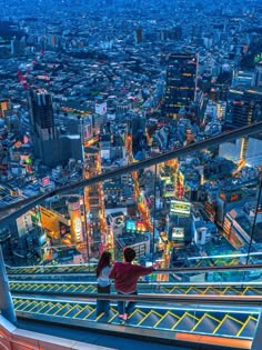 two people standing at the top of a building looking down on a cityscape