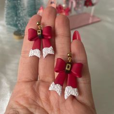 two red and white bows are attached to small earring clips on someone's hand