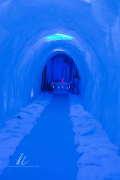 an ice cave with snow on the ground and blue lighting at the entrance to it