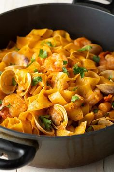 a skillet filled with pasta and clams on top of a wooden table,