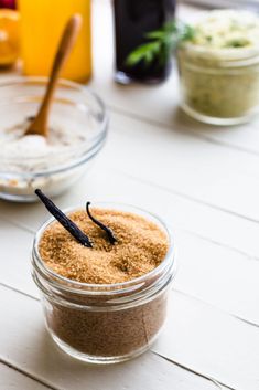 two jars filled with different types of food on top of a white wooden table next to bowls and spoons