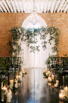 an indoor wedding ceremony with candles and greenery on the aisle, surrounded by brick walls