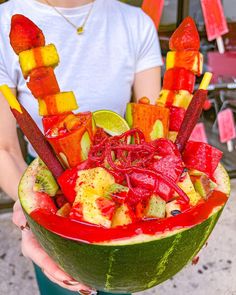 a person holding a watermelon bowl filled with different types of fruits and vegetables