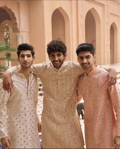 three young men standing next to each other in front of a pink and white building