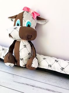 a brown and white stuffed cow sitting on top of a wooden floor next to a wall