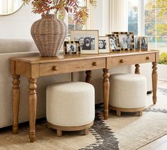 a wooden table topped with pictures and two stools next to a white couch in front of a window