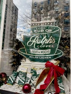 a window display with coffee cups and christmas decorations in the front, behind which is a red bow