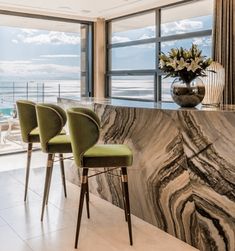 a kitchen with marble counter tops and green chairs next to a large window overlooking the ocean