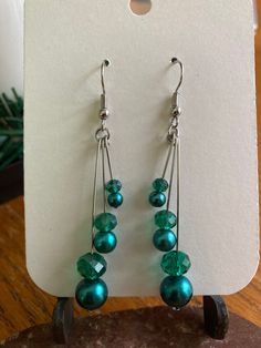 green glass beaded earrings with silver earwires sitting on top of a wooden table