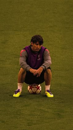 a man sitting on the ground with a soccer ball in his hand and wearing yellow shoes