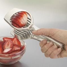 a hand holding a strawberry slicer over a bowl of strawberries with the lid open