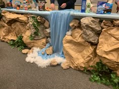 two people standing at a table with paper mache waterfall and rocks on the ground