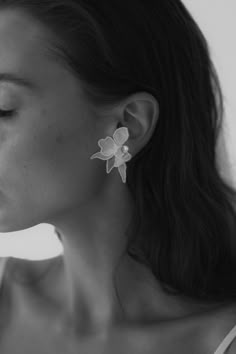 a woman with long hair wearing large white flowers on her ear and earrings in front of her face