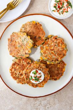 four crab cakes on a white plate next to two plates with gold forks and silverware