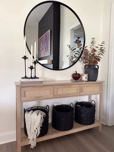 a wooden table with baskets under a round mirror next to a vase and candle holder