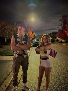 two people are standing on the side of the road at night, one is holding a skateboard