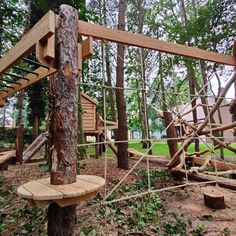 a wooden play area in the woods with swings and climbing ropes attached to it's posts