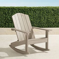 a wooden rocking chair sitting on top of a cement floor next to a green hedge